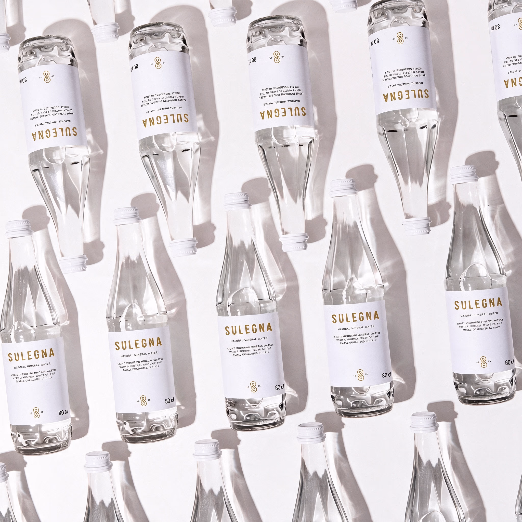 Steklenici SULEGNA Natural, 80 cl in 44 cl, skupaj na toplem nevtralnem ozadju